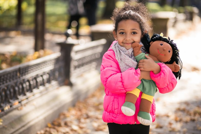 Young black girl holding a doll wearing a winter jacket