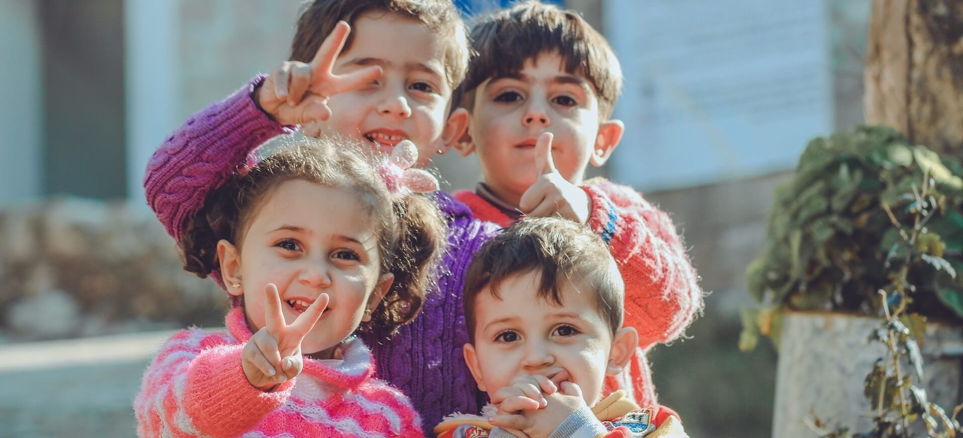 Photo of 4 siblings looking at the camera with a young girl giving the peace sign